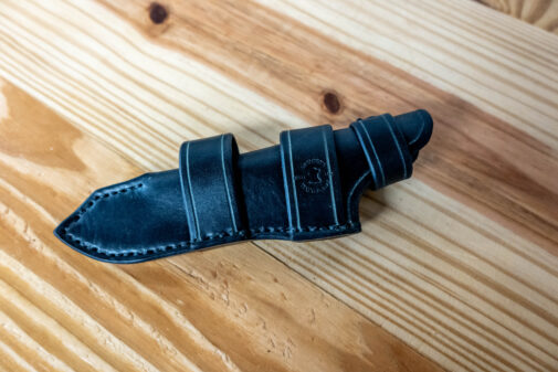 A black Leather Sheath for the Benchmade Fixed Contego sitting on a wooden table.