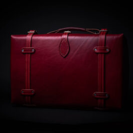 A red Handmade Leather Suitcase sitting in the dark.