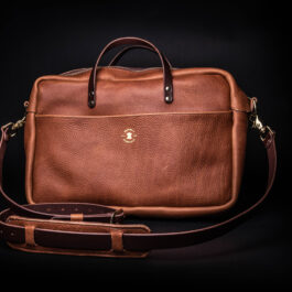 a Horween Leather Briefcase Satchel with a brown strap on a black background.
