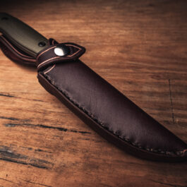 A Handmade Leather Sheath for the Benchmade Anonimus on a wooden table.