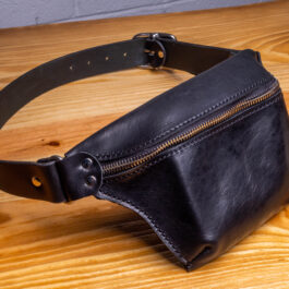 A black leather fanny pack on a wooden table