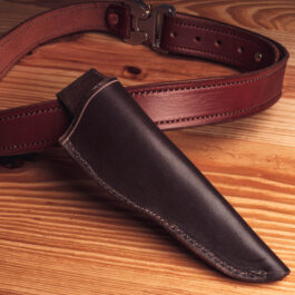 A Handmade Leather Sheath attached to a leather belt on a wooden surface.
