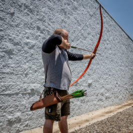 A man holding a Ranger Hip Quiver and a bow in front of a wall.