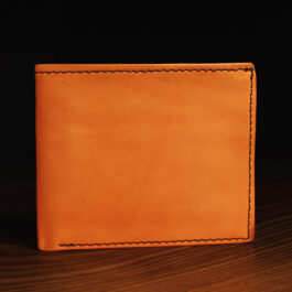 A Hermann Oak Bifold Leather Wallet With Hemmed Edge sitting on top of a wooden table.